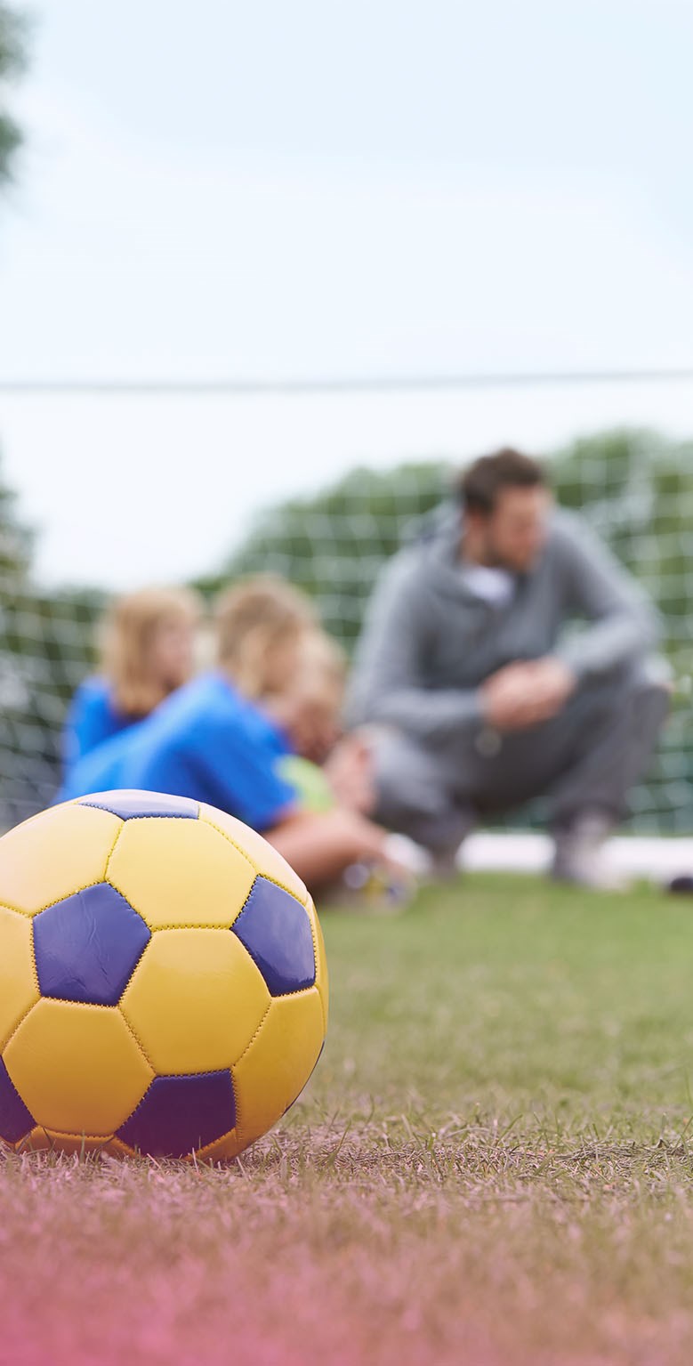 Fotboll i förgrunden med ett fotbollslag med ledare i bakgrunden
