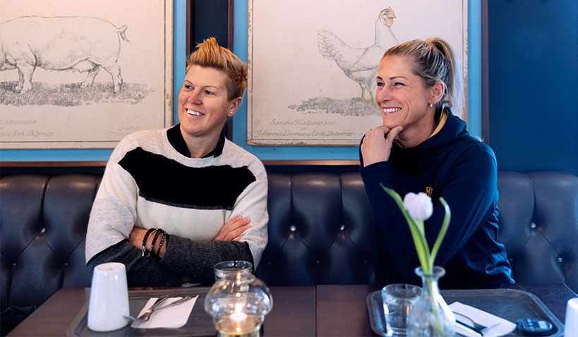Hockeyprofilen Erika Holst sitter bredvid Erica Johansson i en soffa.