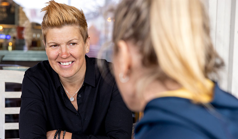 Erika Holst sitter mitt emot en ljushårig kvinna med uppsatt hår. 
