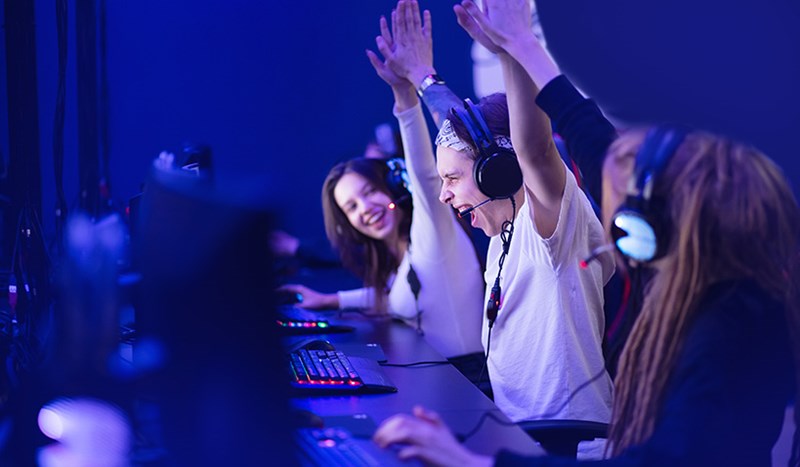 Tre unga personer gör high five framför datorskärmar på e-sportsturnering