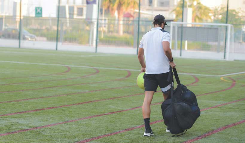 En tränare som bär bollar på fotbollsplan
