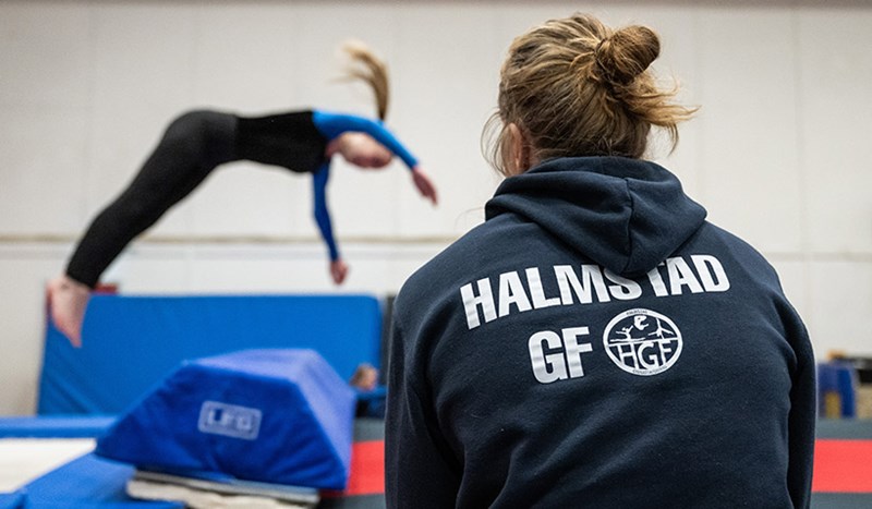 Flicka gör volt på tjockmatta i gymnastiksal framför ledare i Halmstads Gymnastikförening