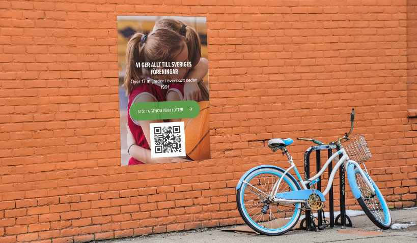En orange tegelvägg med cykel lutad emot och affisch med QR-kod