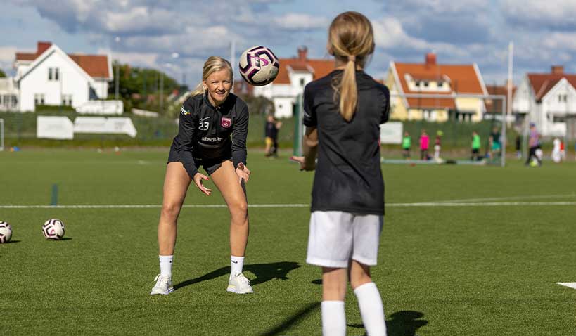 Två fotbollsspelare kastar boll till varandra på gräsplan