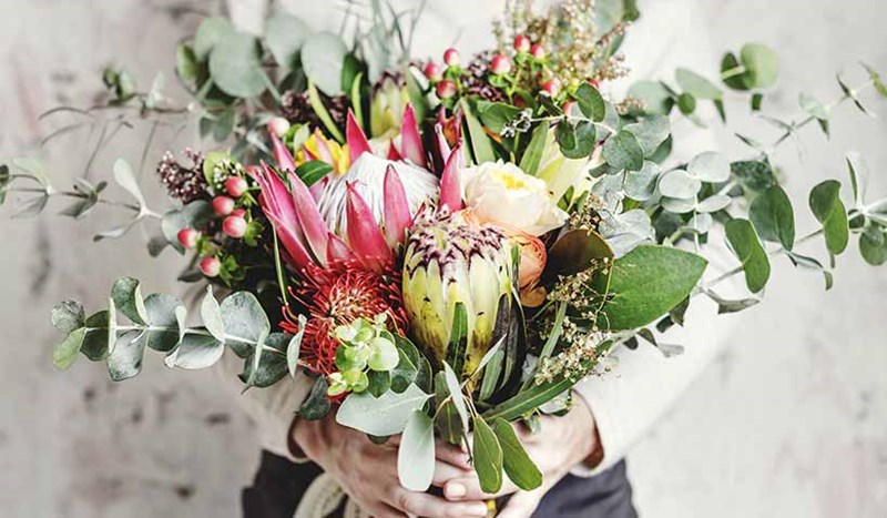 En blombukett som hålls fram av kvinna i vit tröja
