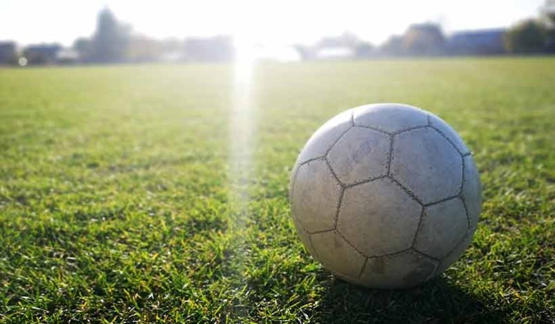 En utsliten vit fotboll i solsken på gräsplan