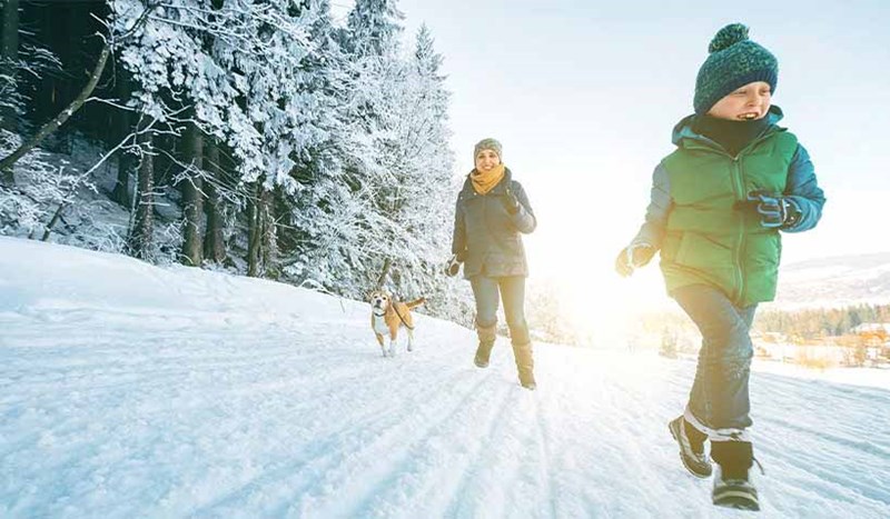 Mamma och son springer med sin hund i snöig backe