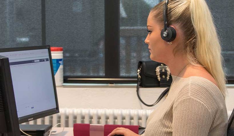 Glad tjej som jobbar framför dator med headset
